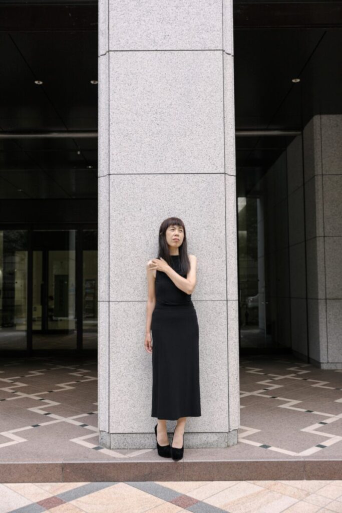 黒のタイトロングを纏い都会の中に立つエイジレスモデル。無駄のないミニマルな静けさが際立つ1枚。